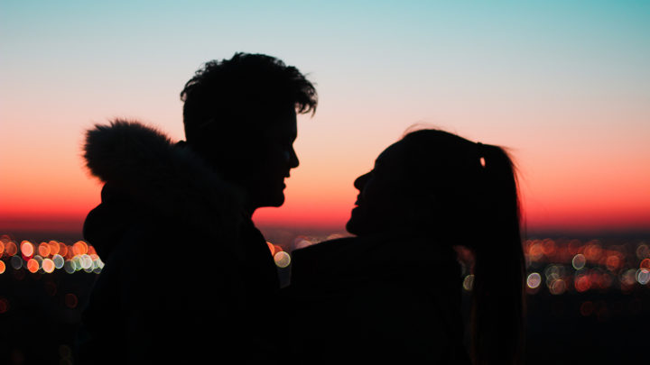 Two people embrace in the foreground of a cityscape
