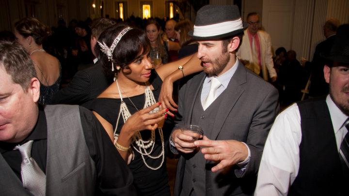 A couple dressed in Prohibition era clothing chatting and having drinks